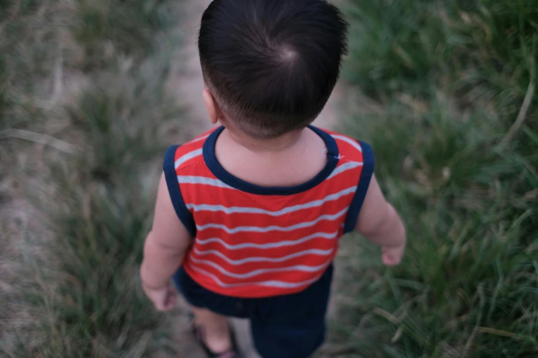 a toddler standing in a field with his arm around his back