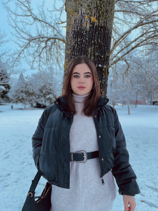 a woman standing next to a tree in the snow