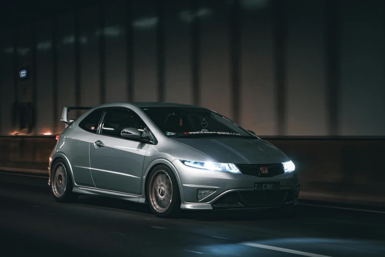 a silver honda civic hatch driving down a dark street