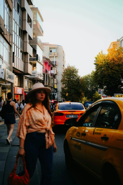 the young woman in the hat is standing in front of some taxis