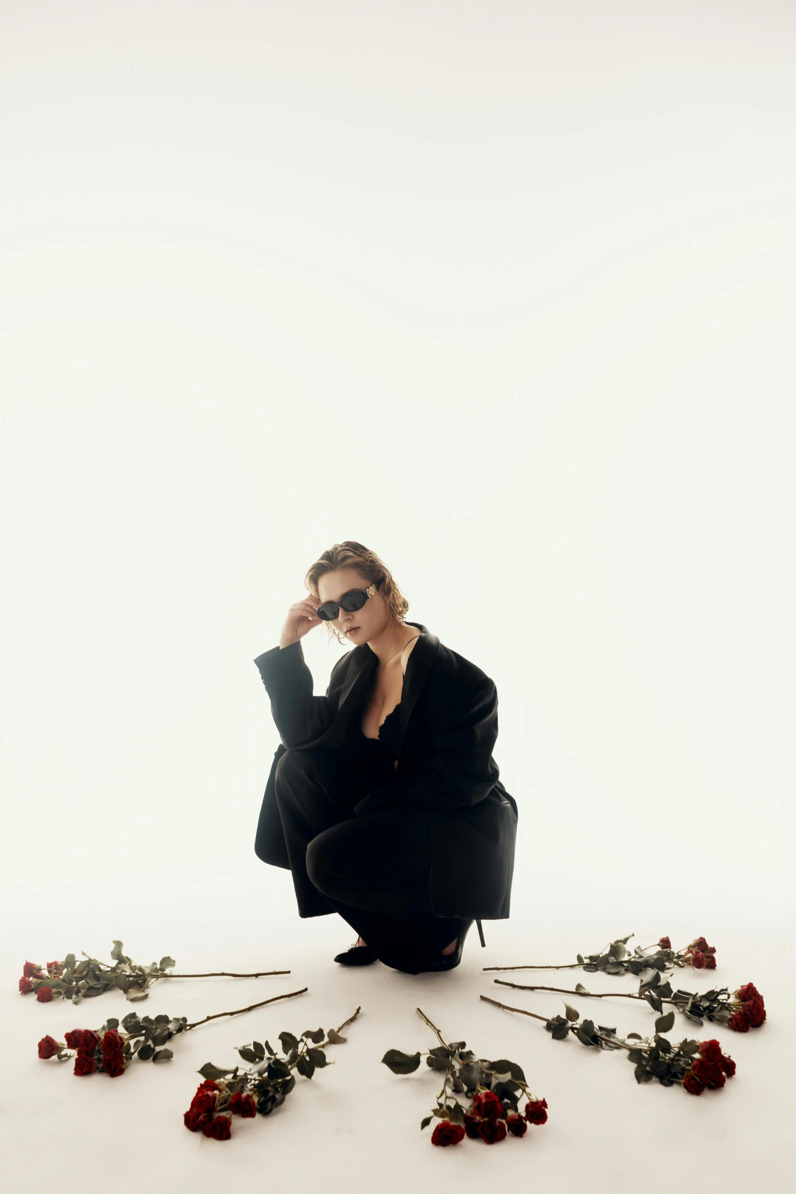 a woman in black is sitting on a white background, surrounded by flowers