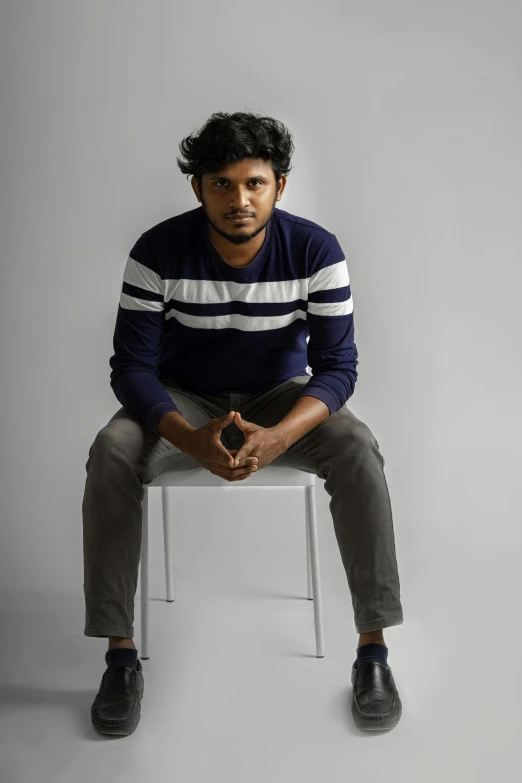 a young man sits on a white chair while posing for a po