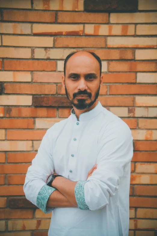 a man with his arms crossed next to a brick wall