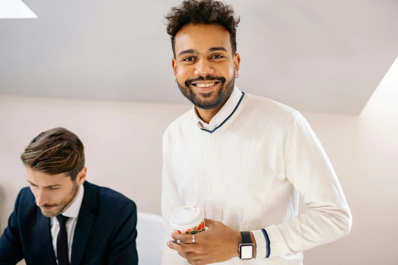 a man with beard and white sweater holding a drink