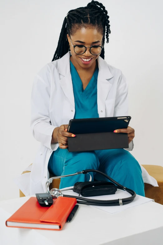 a woman with glasses sitting on a desk, holding a tablet