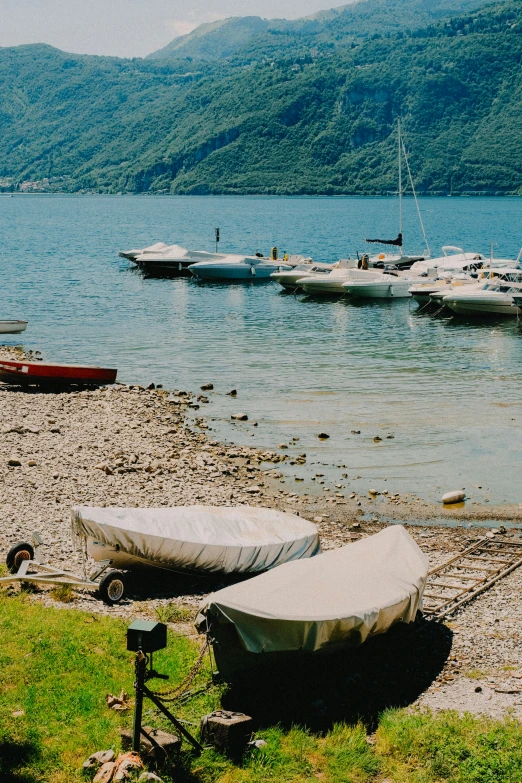 boats docked near a sandy shore, with mountains in the background