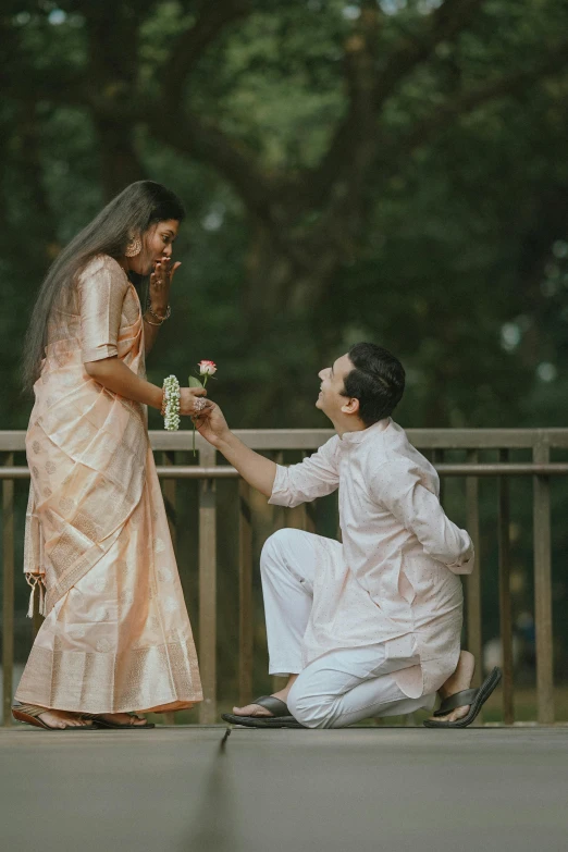 two people in white and gold outfits exchanging a flower