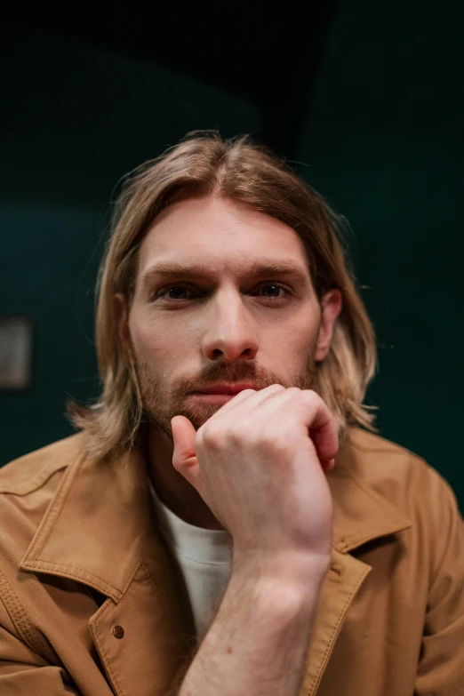 a man in an orange jacket staring at the camera with his hand on his chin