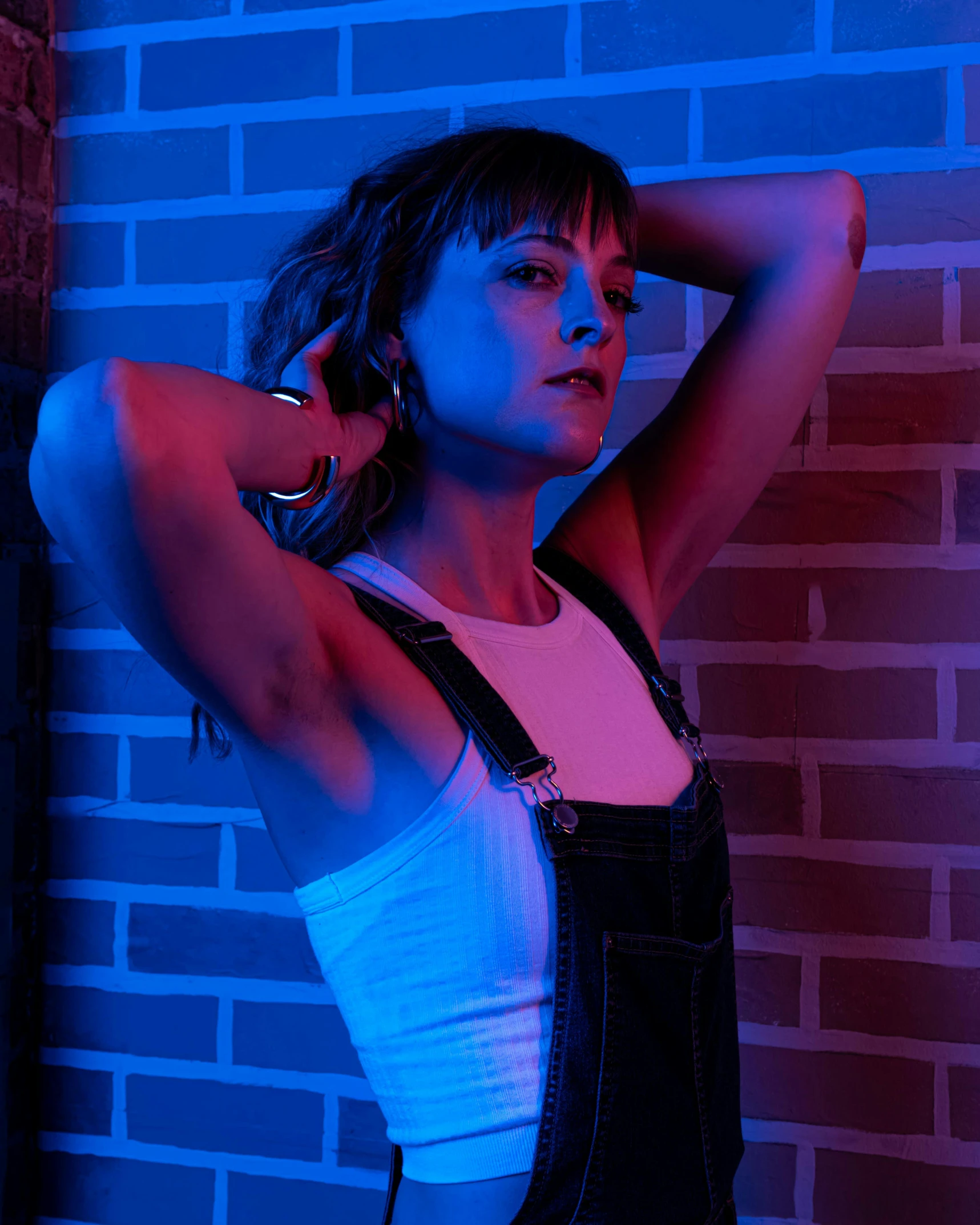 woman in black overalls and tank top leaning against brick wall