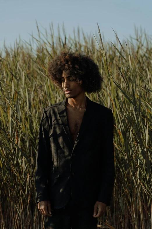 a black man wearing a dark shirt and standing in front of a field of plants