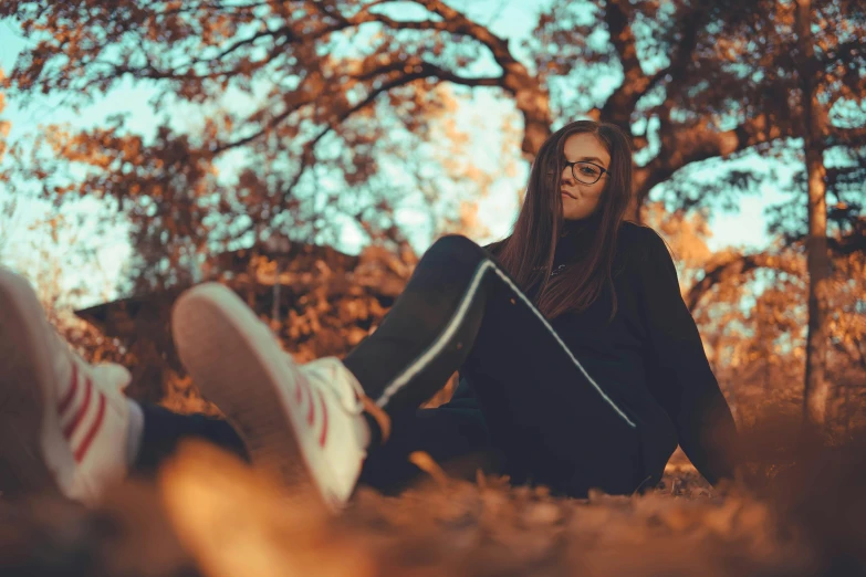 a woman is sitting in the grass wearing a sweater and jeans