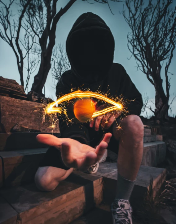 a man in a hoodie is using an electronic device to burn some sparks on his hands