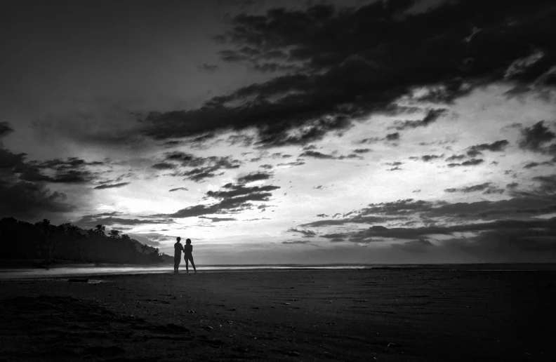 a couple walks on the beach under an almost cloudy sky