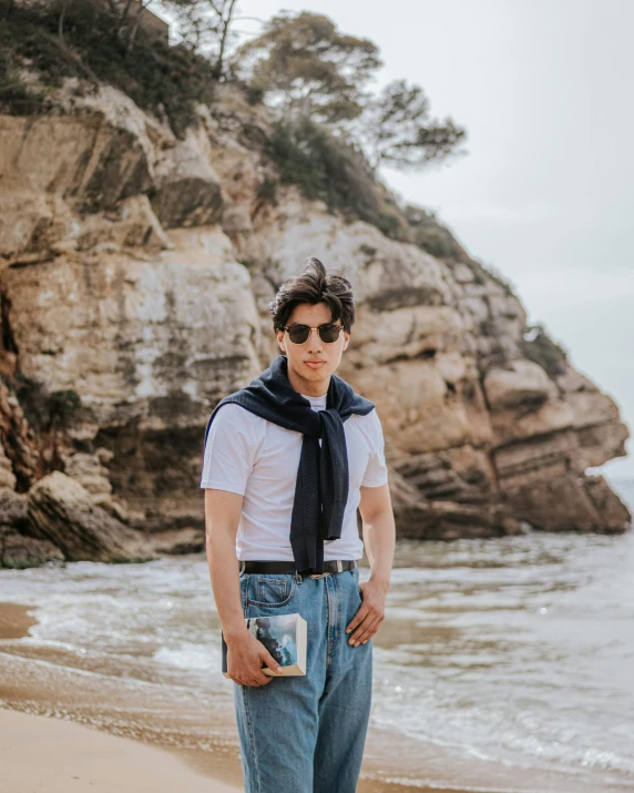 the man stands in the sand by the beach and is wearing glasses