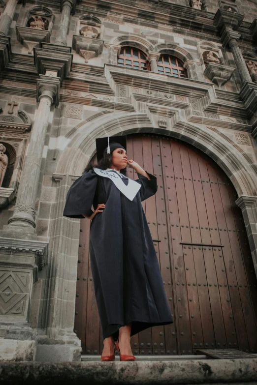 woman in graduation gown looking up at large building