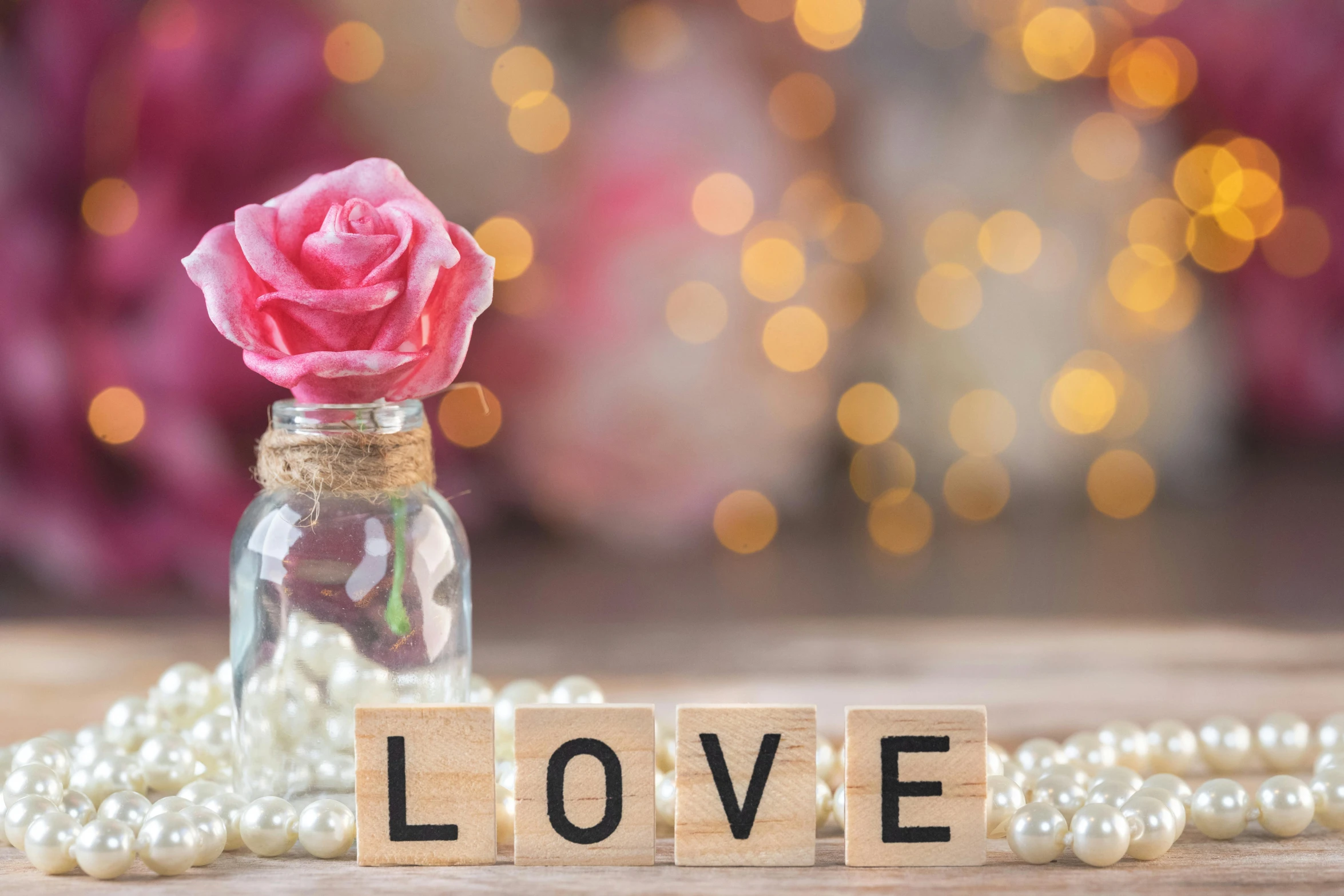 the word love written in wooden blocks beside a pink rose and pearls