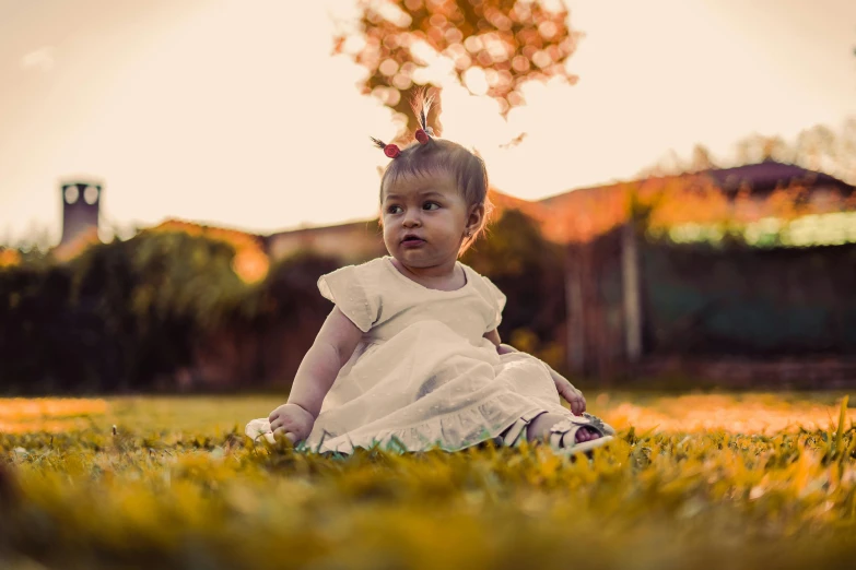 an adorable baby is sitting on the ground near the grass