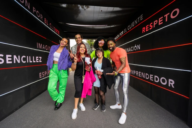 six people in brightly colored outfits are posing on a red and black background