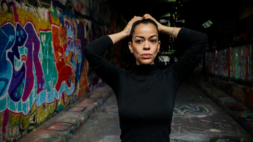 a woman in black standing next to a graffiti covered wall