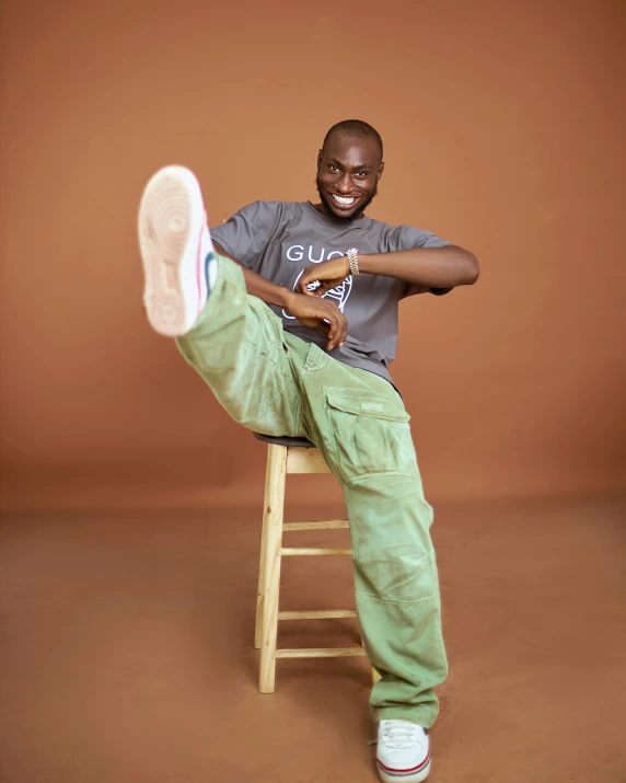 a smiling black man holding a shoe while sitting on a stool