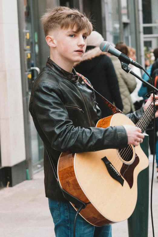 a boy holding a guitar on top of a city street