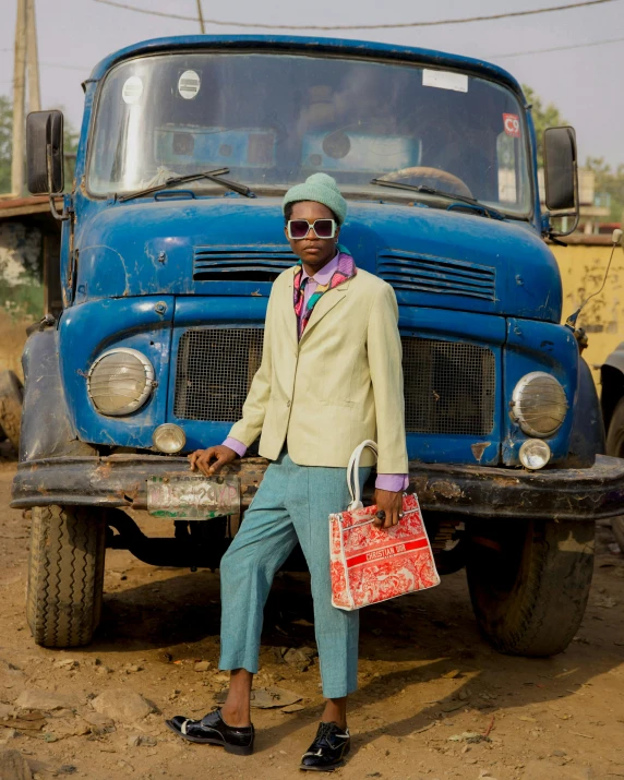 man in suit standing by the front of a blue truck