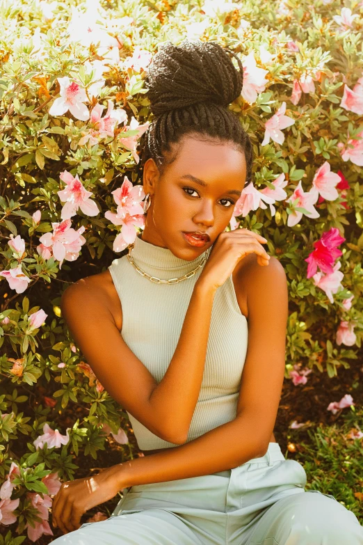 a black woman sits against flowers while looking off to the side