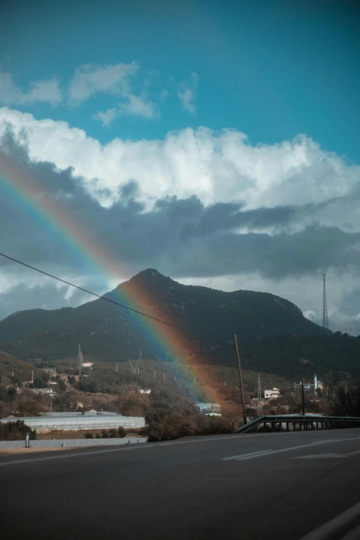 rainbow appearing in cloudy sky over road with mountains behind