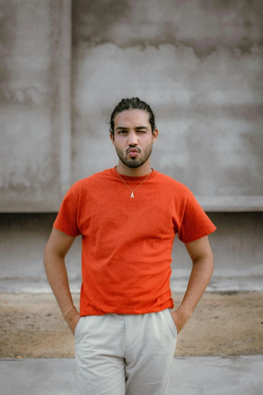 a man in an orange shirt and tan pants standing by concrete blocks