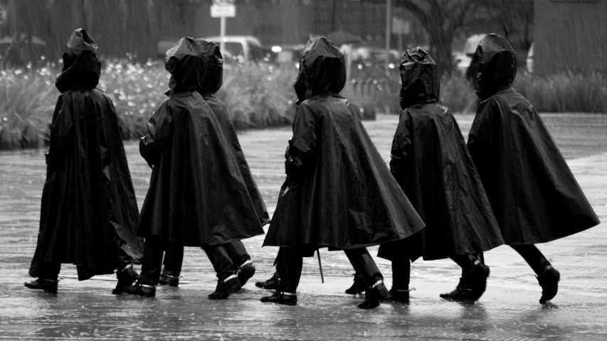 four people in hooded coats walk through the rain