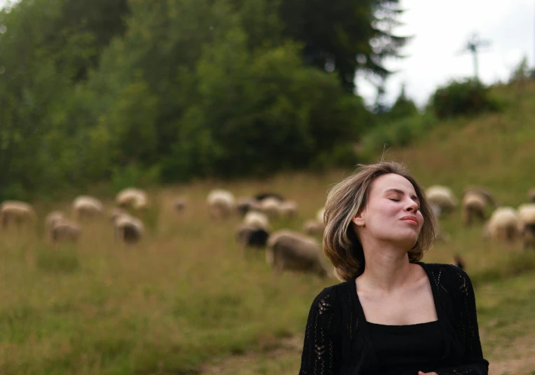 a woman standing in a field with lots of sheep