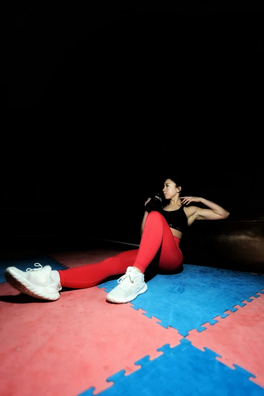 a woman in a red top, pants and white sneakers sits on a bright blue mat