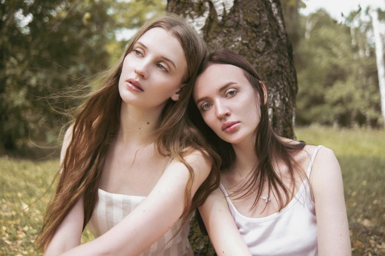 two girls are sitting under a tree with their arms around each other