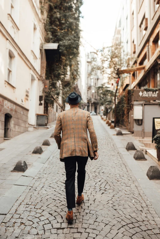 man walking through town in brown jacket and plaid shirt