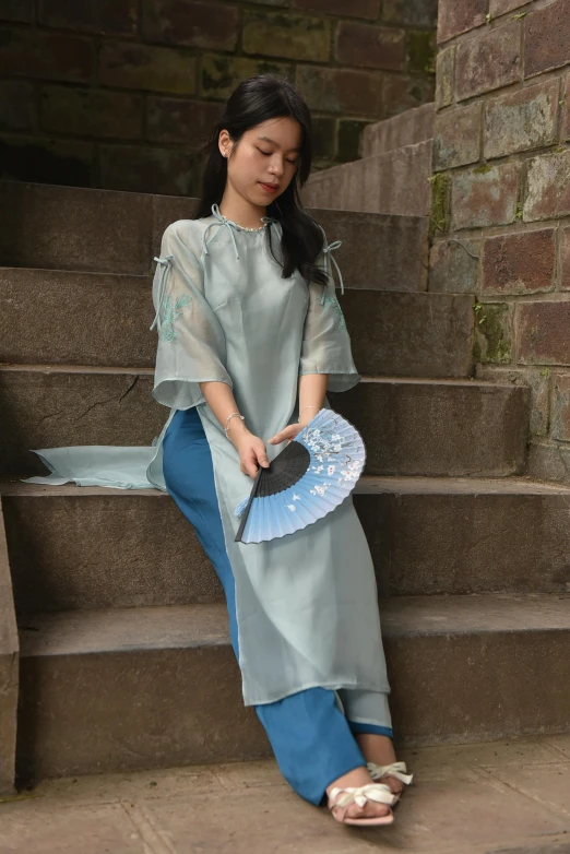 woman in long light gray outfit sitting on a staircase with a hat