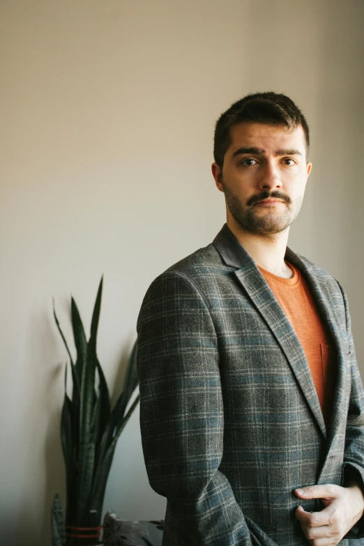 a man in a grey suit stands near a plant