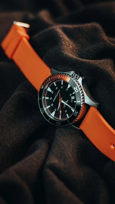 a watch with an orange band on top of brown fabric