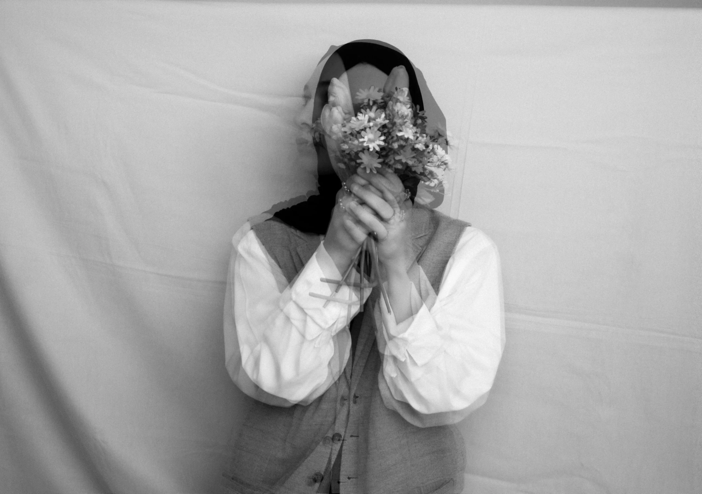 man hiding in sweatshirt holding flowers in front of face