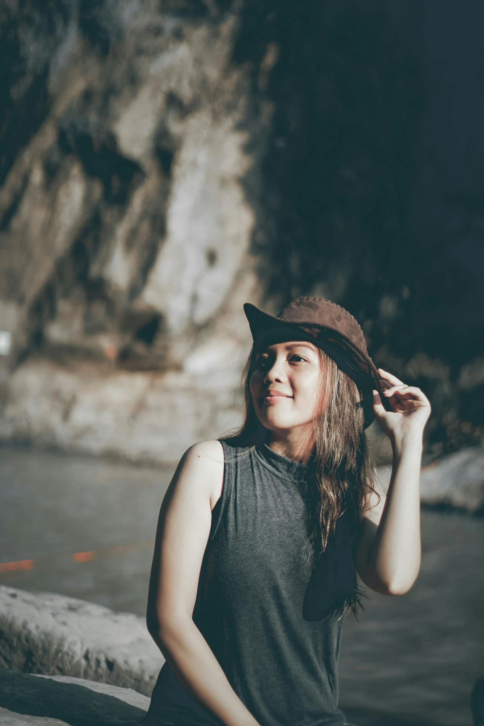 a woman sitting on rocks next to the water wearing a hat