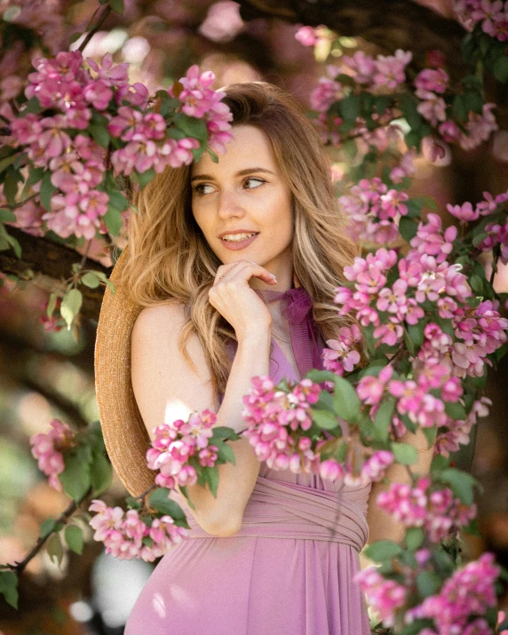 the woman wearing a purple dress is under a flower - covered tree