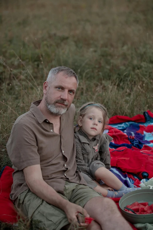 an older man and young child sitting on a blanket outdoors