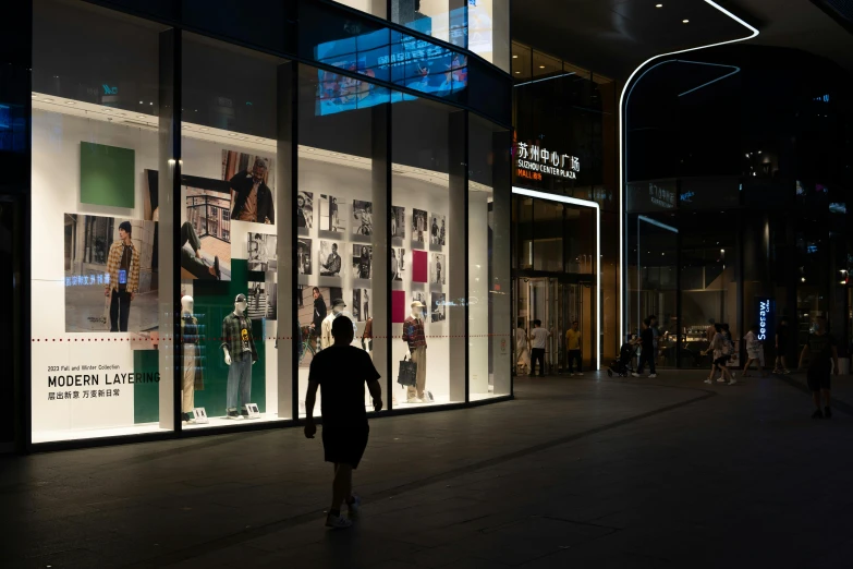 people walk in front of a fashion store at night