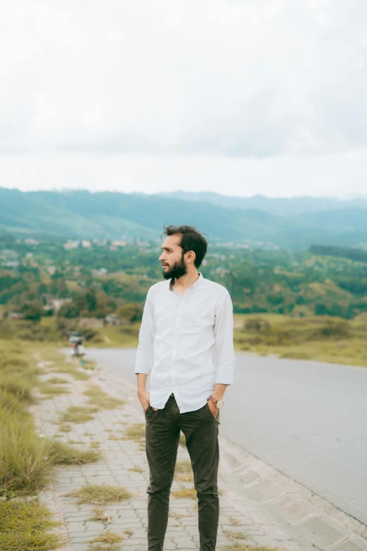 a man with a beard and white shirt standing on a hill