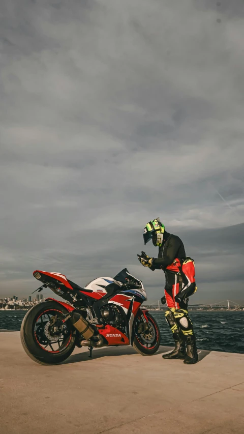 a man with a helmet and gear standing next to a red motorcycle