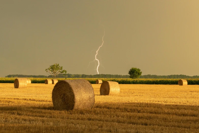 a lightning bolt is in the sky behind bales of hay