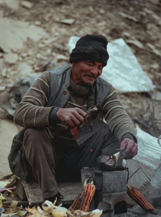 a man with a hat sitting next to a camping stove