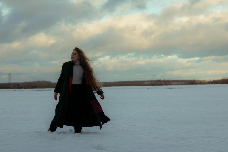 the woman walks through snow while wearing a long coat