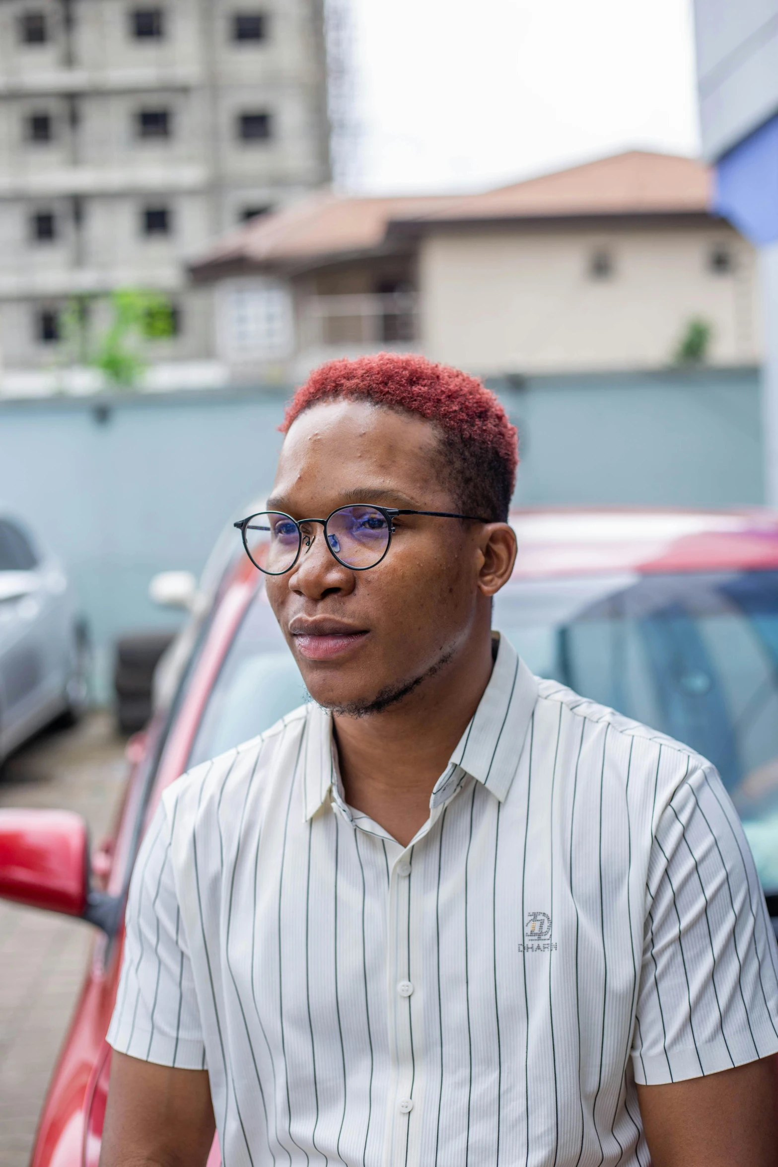 a man with red hair and glasses standing near cars