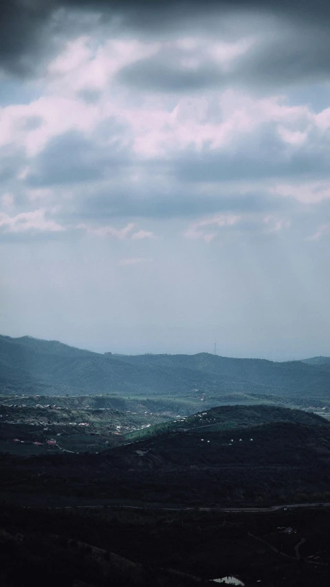 an airplane is flying over the hills under a cloudy sky