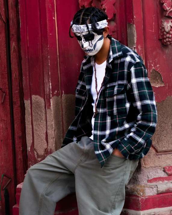 man in plaid shirt and bandanna sitting against red wall